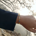 Gold bracelet with evil eye protection stones on a wrist against a natural background
