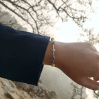 Gold bracelet with evil eye protection stones on a wrist against a natural background