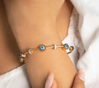 Gold bracelet with blue and clear gemstones on a wrist against a white background